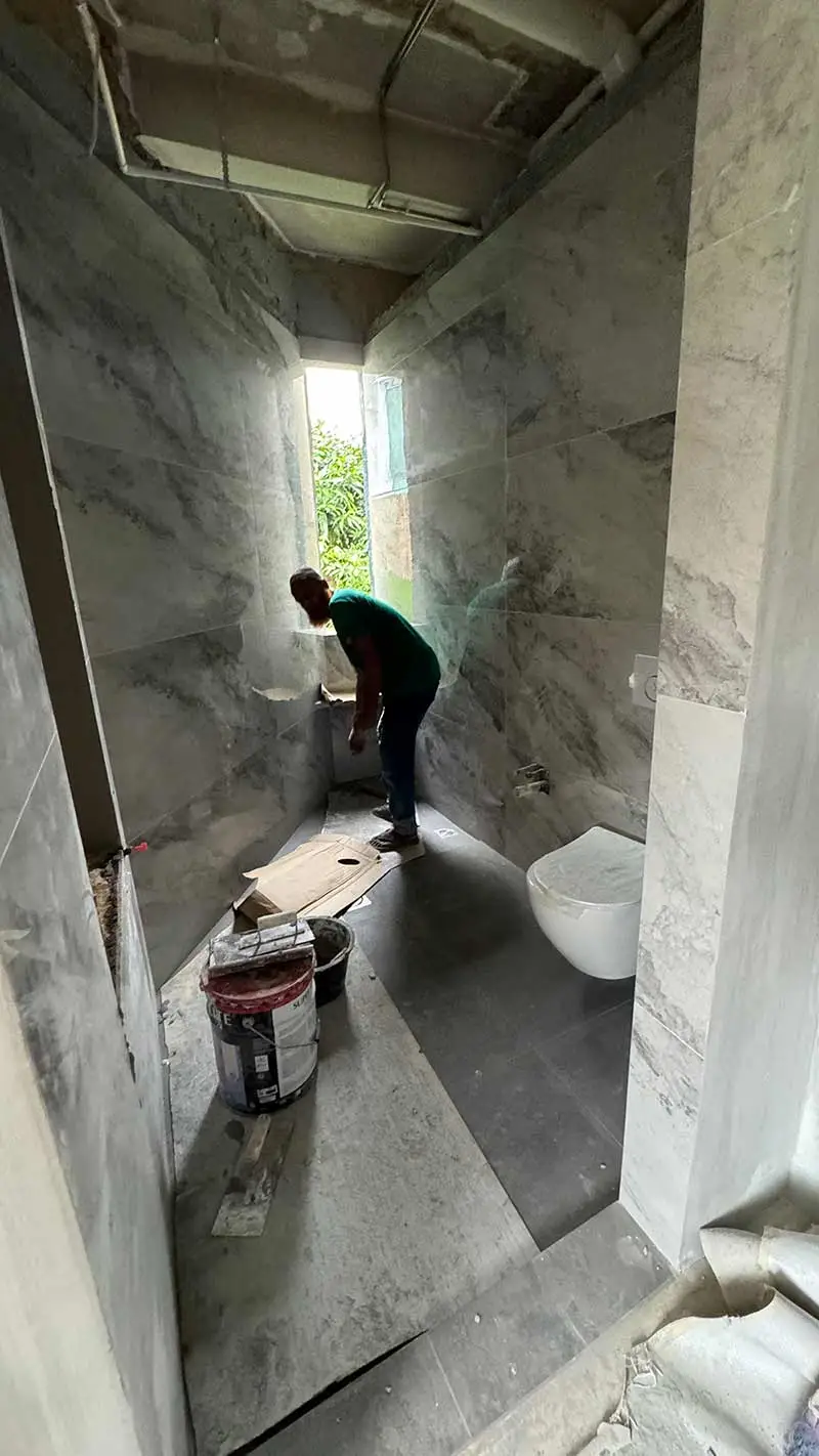 A worker installing a toilet in a small bathroom with gray marble-look tiles, depicting a Home Renovation in Singapore.