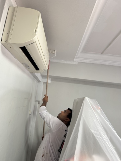 Everyday Renovation painter doing detailed Nippon Odour-less Painting Service near AC unit in Singapore, affecting project cost.